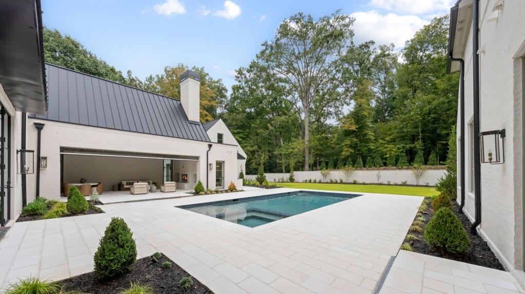 Courtyard pool with pale stone patio, covered seating area, and mature trees beyond the garden wall.