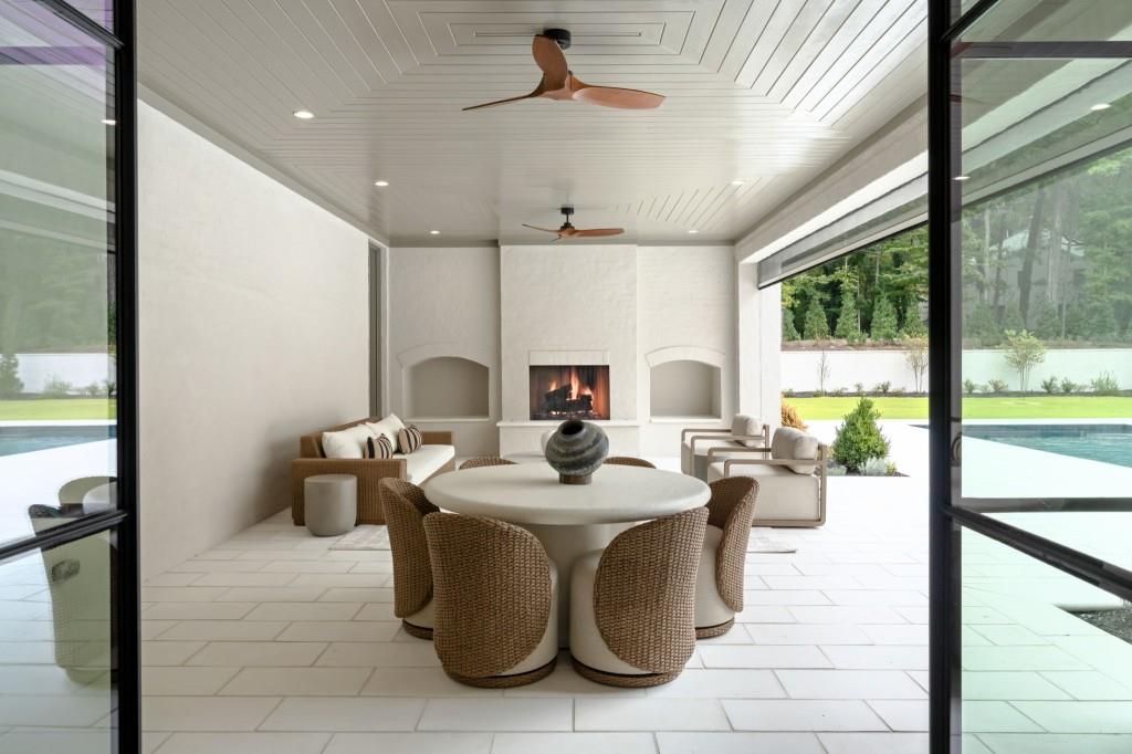 Covered patio with a fireplace, wicker dining set, and views of the pool and landscaped yard.