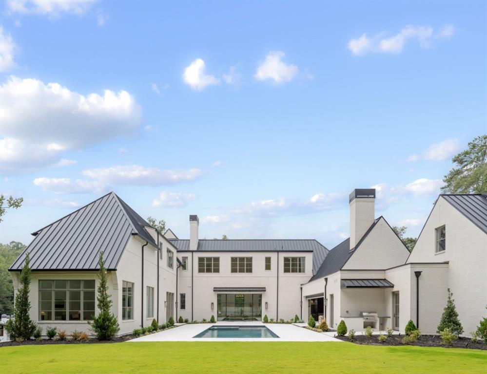 Modern white-brick home surrounding a rectangular pool and stone patio, with a broad green lawn.