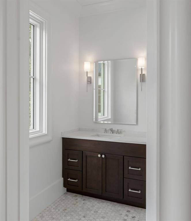 Bathroom with dark wood vanity, white hex tile floor, tall window, and mirror flanked by sconces.