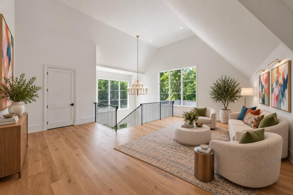 Upstairs living area with a vaulted ceiling, tree views, and a bright seating area beside the stair railing.