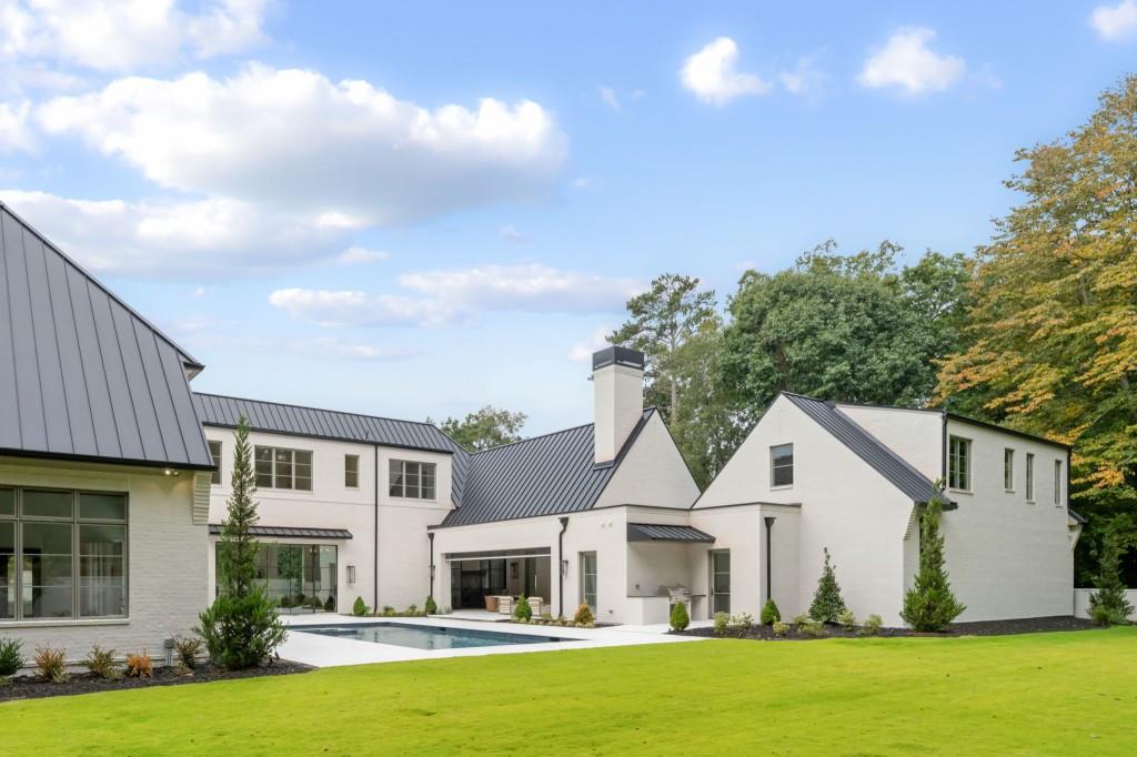 Modern white house with dark metal roofs, a courtyard pool, and a broad green lawn.