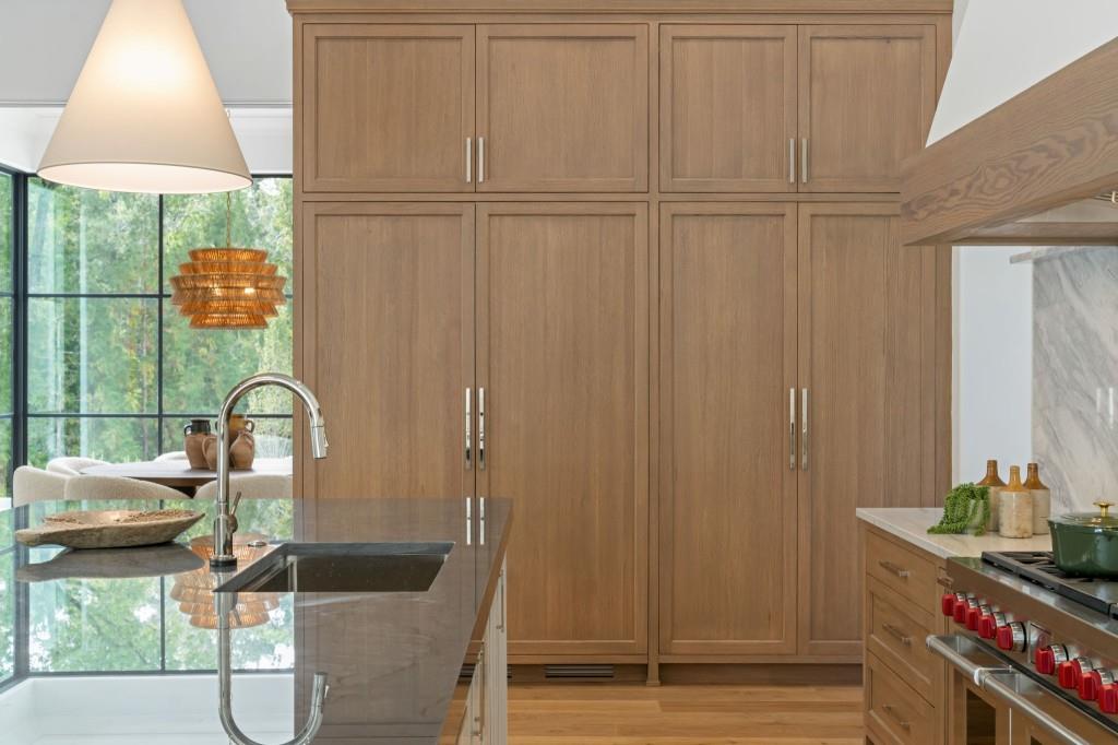 Kitchen with warm wood cabinetry, a stone island, and large windows overlooking greenery.