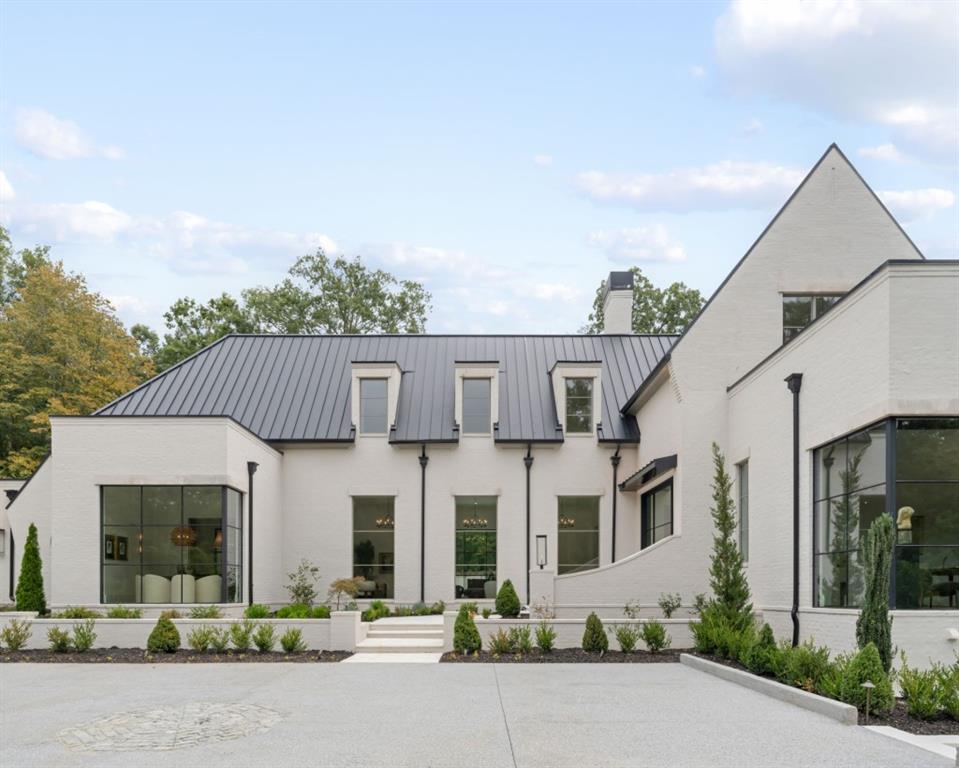 Modern white brick home with a steep gable, dark metal roof, and landscaped driveway.