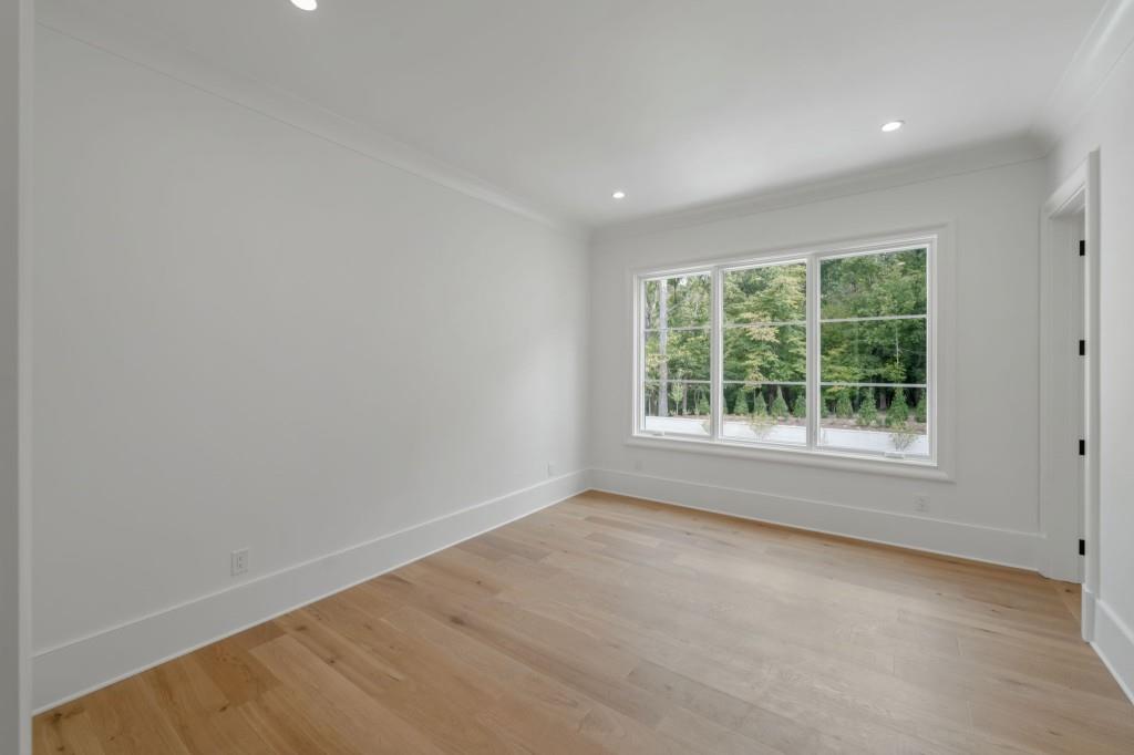 Empty room with light hardwood floors and a wide window overlooking trees.