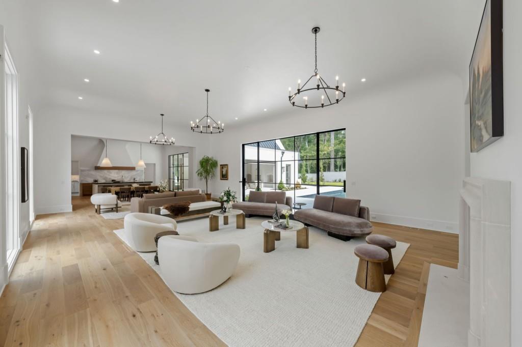 Open-plan living room with high ceilings, contemporary seating, pale wood floors, and glass doors to a patio.