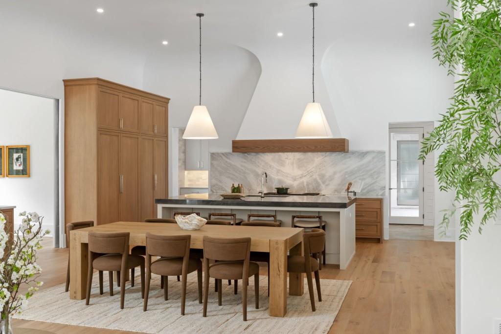 Open kitchen and dining area with wood cabinetry, marble backsplash, and a long dining table.