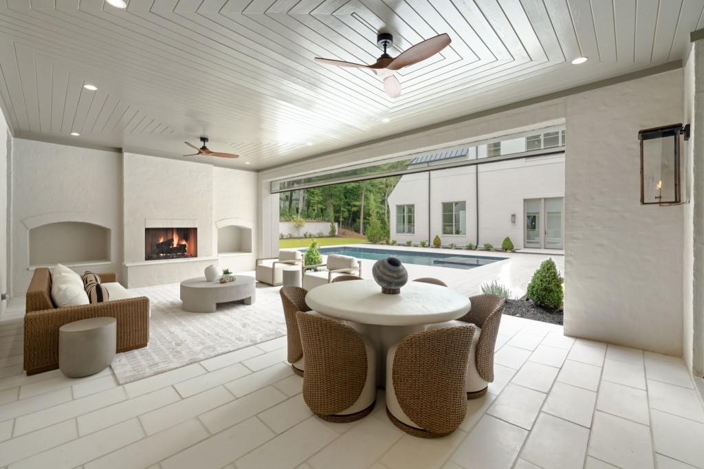 Covered patio with dining set and fireplace overlooking a swimming pool.