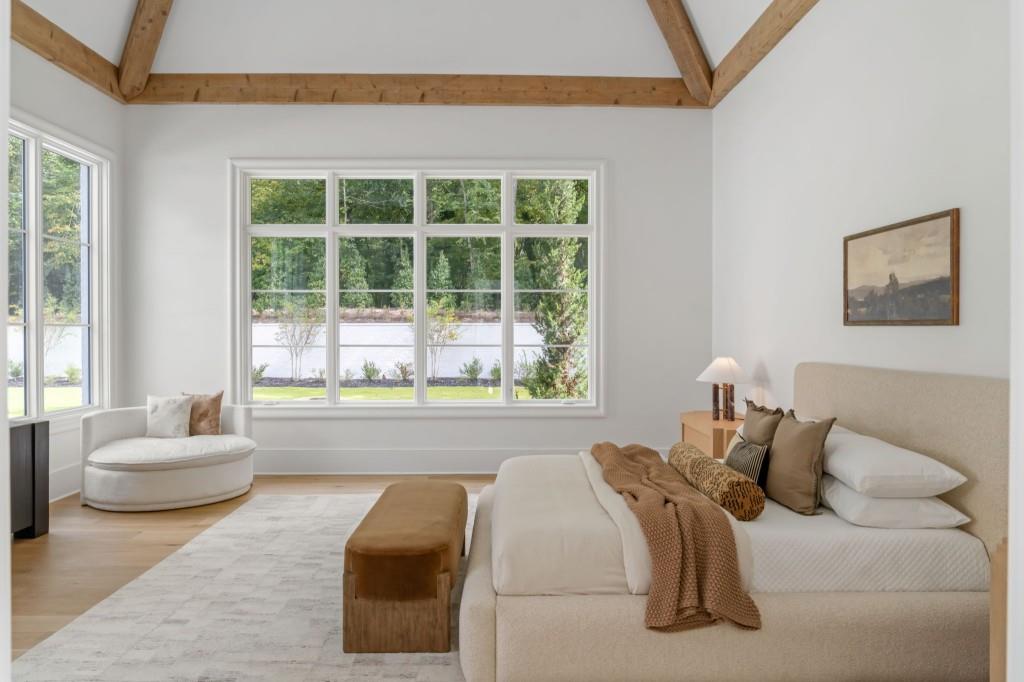 Staged bedroom with exposed wood ceiling beams and broad windows overlooking greenery.