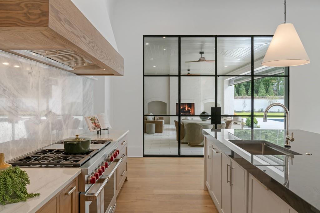 Modern kitchen with marble backsplash, a large gas range, and black-framed glass partitions to the living room.