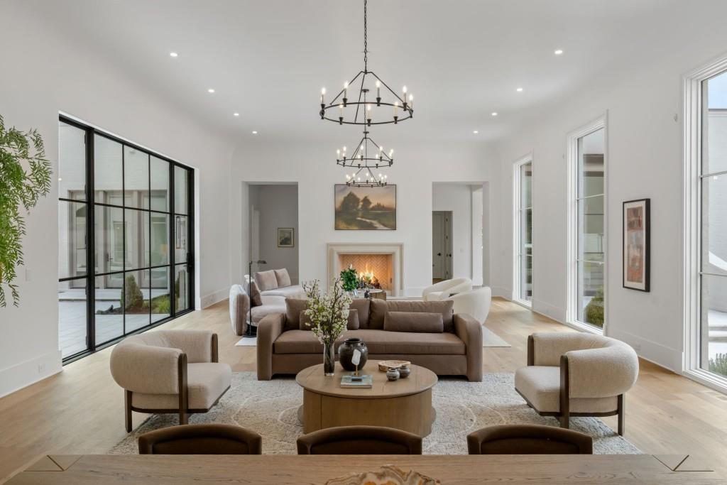 Staged living room with a fireplace, black-framed glass doors, and two ring chandeliers.