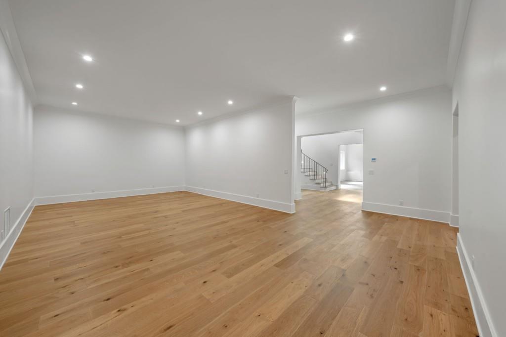 Empty room with light oak floors and recessed lighting, opening to a hall with a staircase.