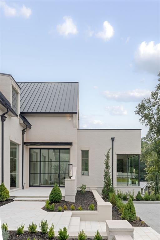 Modern white house with a dark metal roof, expansive glass doors, and a landscaped stone patio.