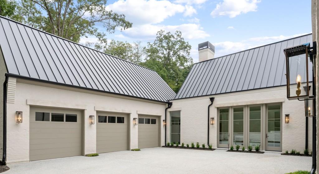 White-brick home courtyard with three garage doors and standing-seam metal roofs.