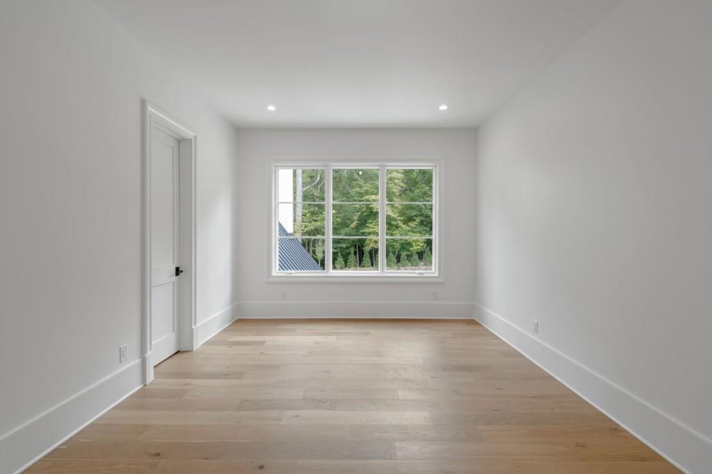 Empty bright room with pale hardwood floors and a large window overlooking trees.
