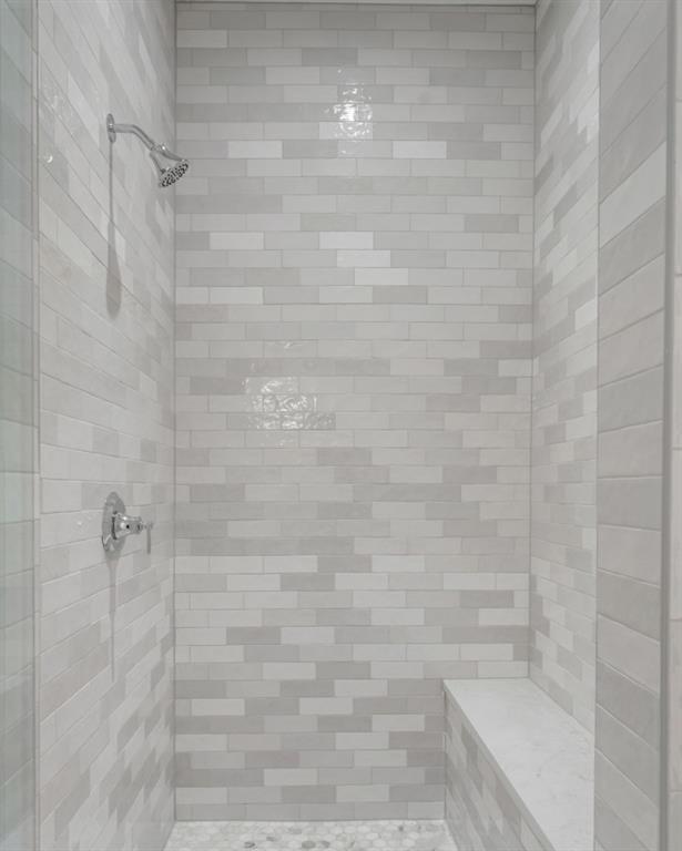 Walk-in shower with gray tile walls, a built-in bench, and pebble flooring.