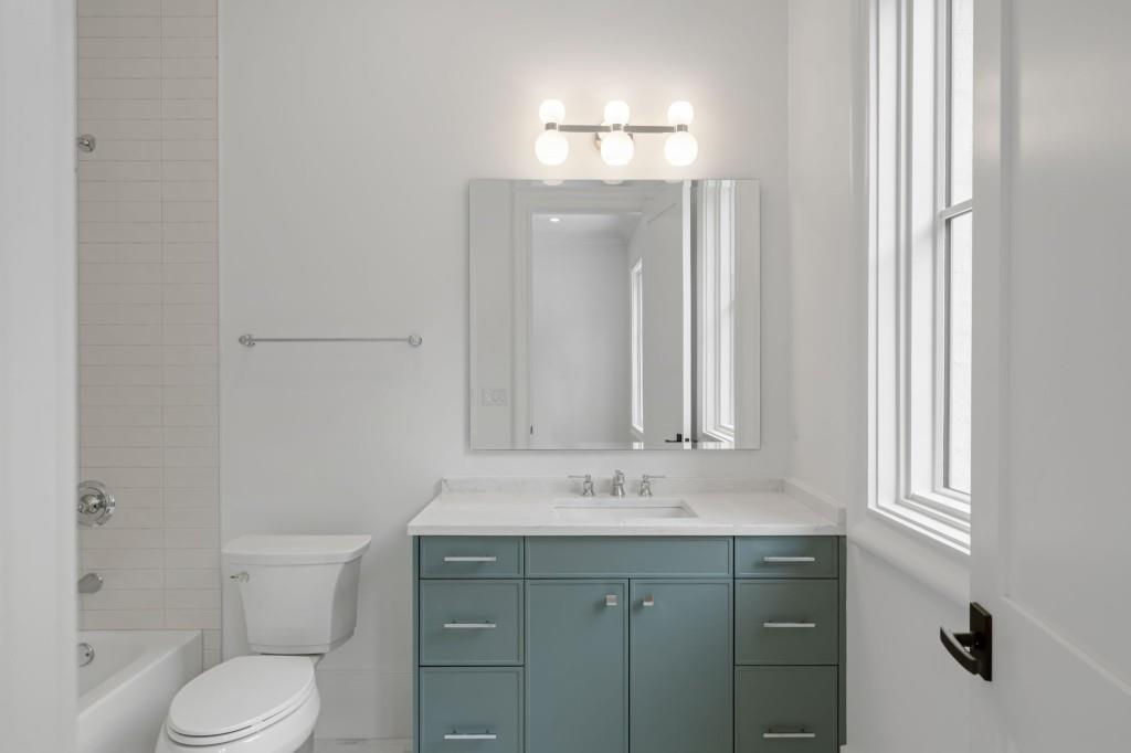 Bathroom with a blue-green vanity, white bathtub, tiled shower, and tall windows.