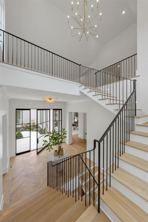 Double-height foyer with a sweeping wood staircase, black railings, and a sculptural chandelier.
