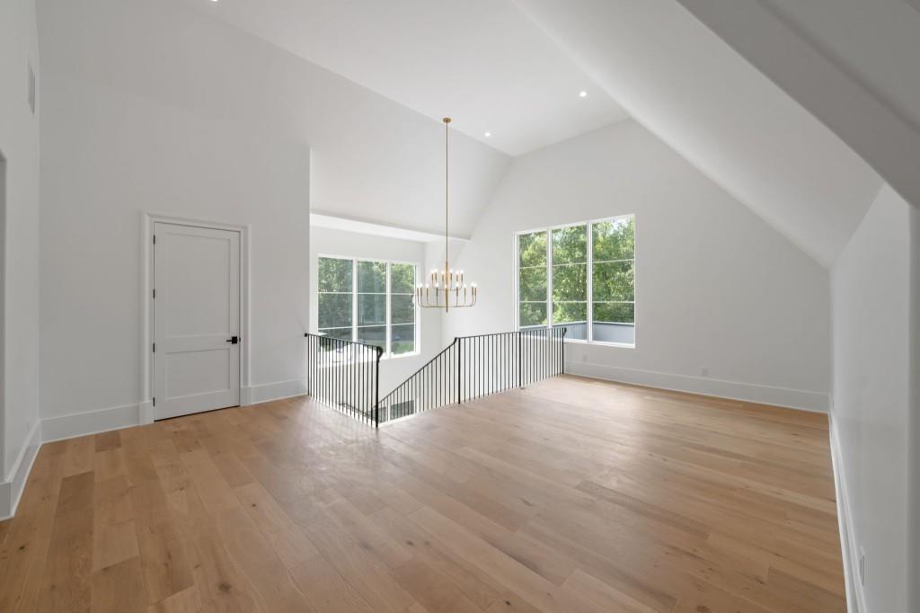 Vacant upstairs room with vaulted ceiling, hardwood floors, large windows, and a stairwell railing.