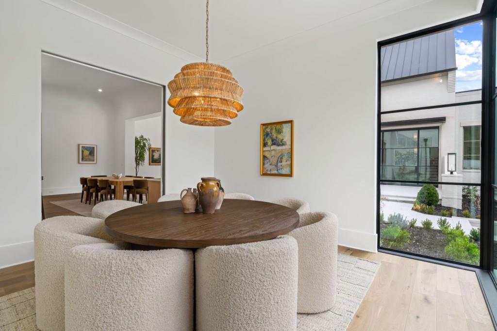 Dining area with a round wood table, cream chairs, woven pendant, and large window.
