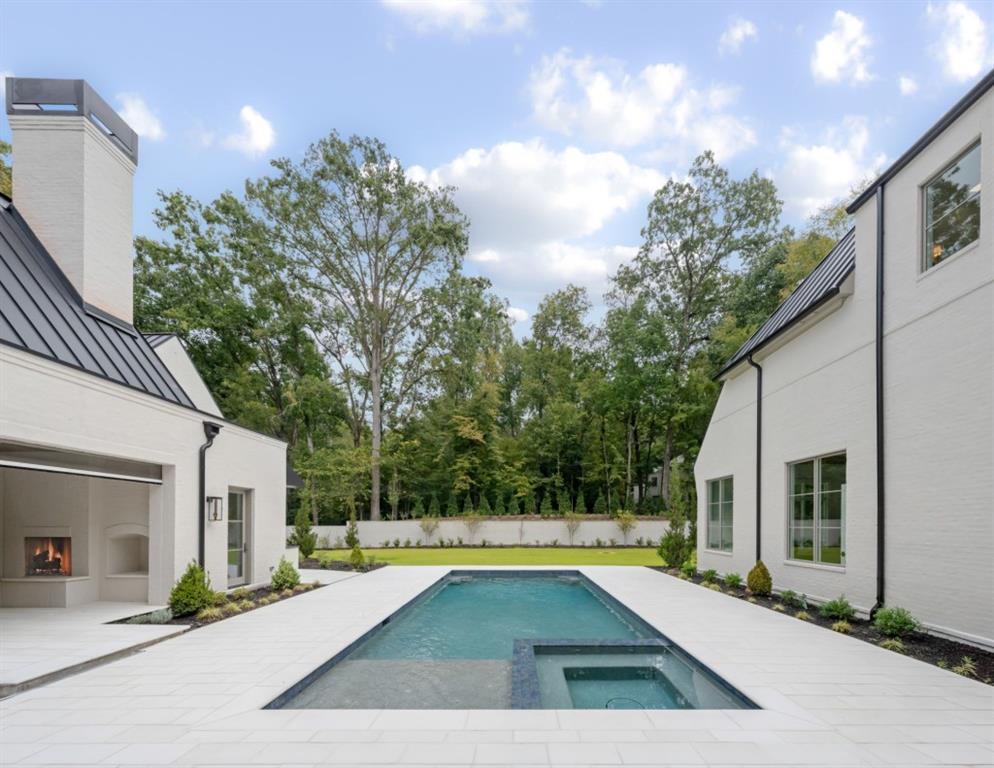 Swimming pool and spa in a courtyard between white-brick wings of a modern home.