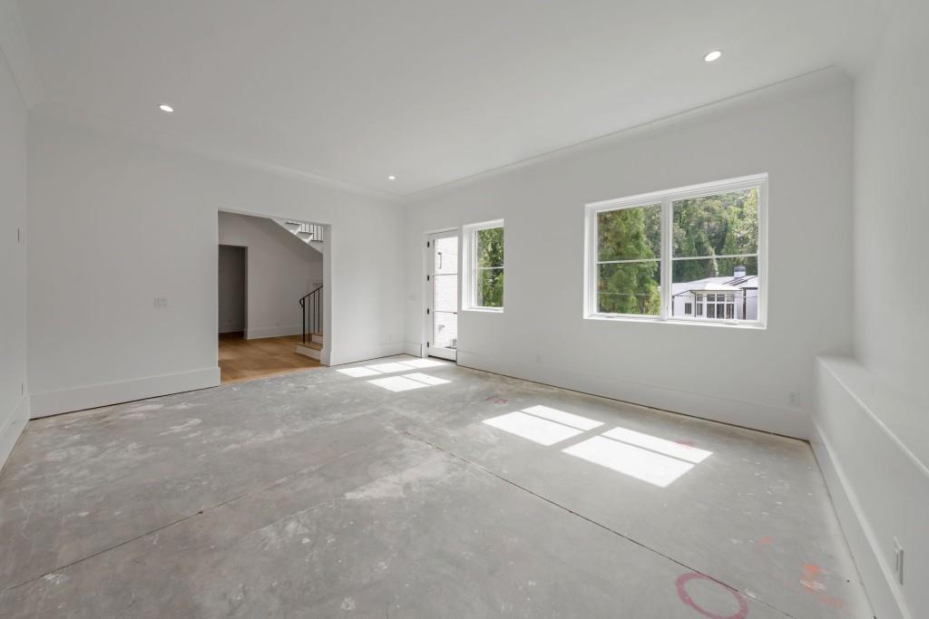 Unfinished room with a bare concrete floor, recessed lights, and large windows overlooking trees.