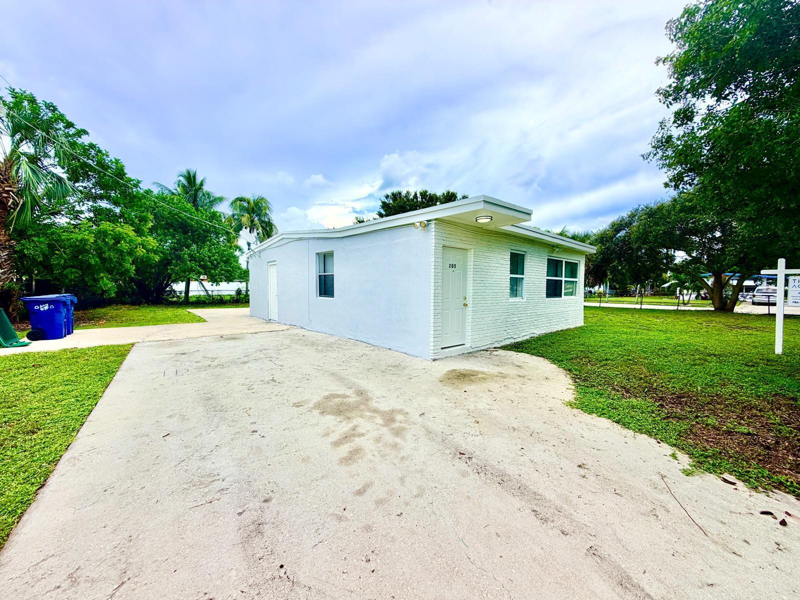 White single-story property with a flat roof, brick facade, and broad concrete driveway.