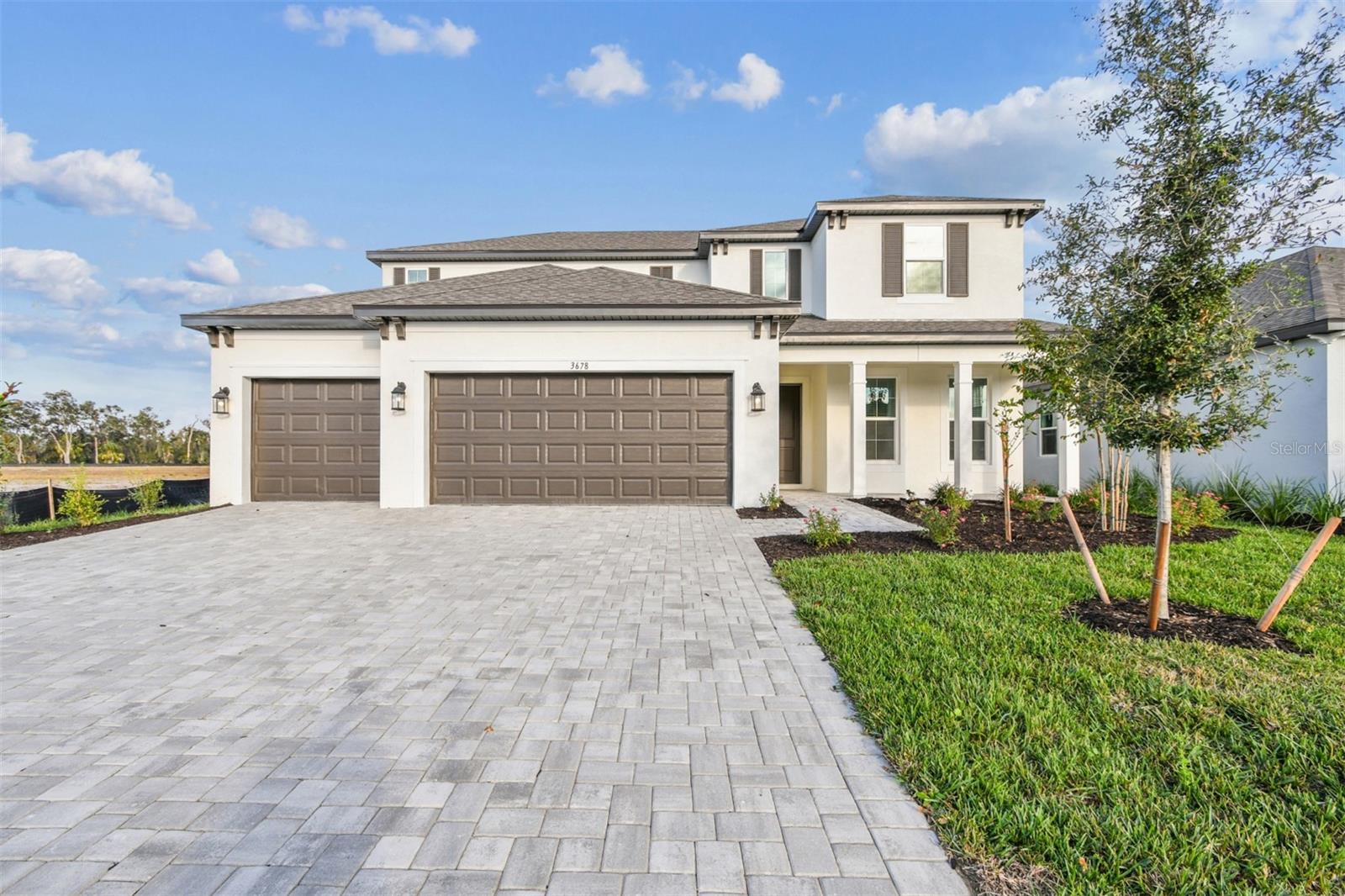 Two-story white home with dark garage doors, a wide paver driveway, and a landscaped front lawn.