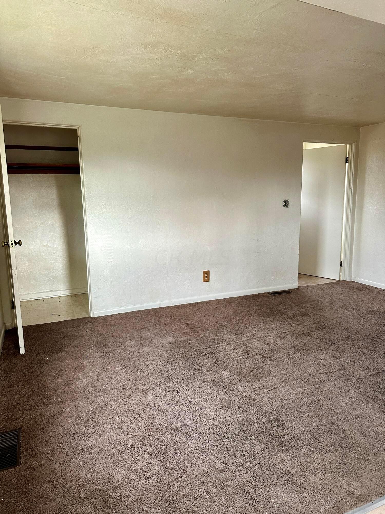 Vacant bedroom with brown carpet, an open closet, and a doorway to an adjoining room.