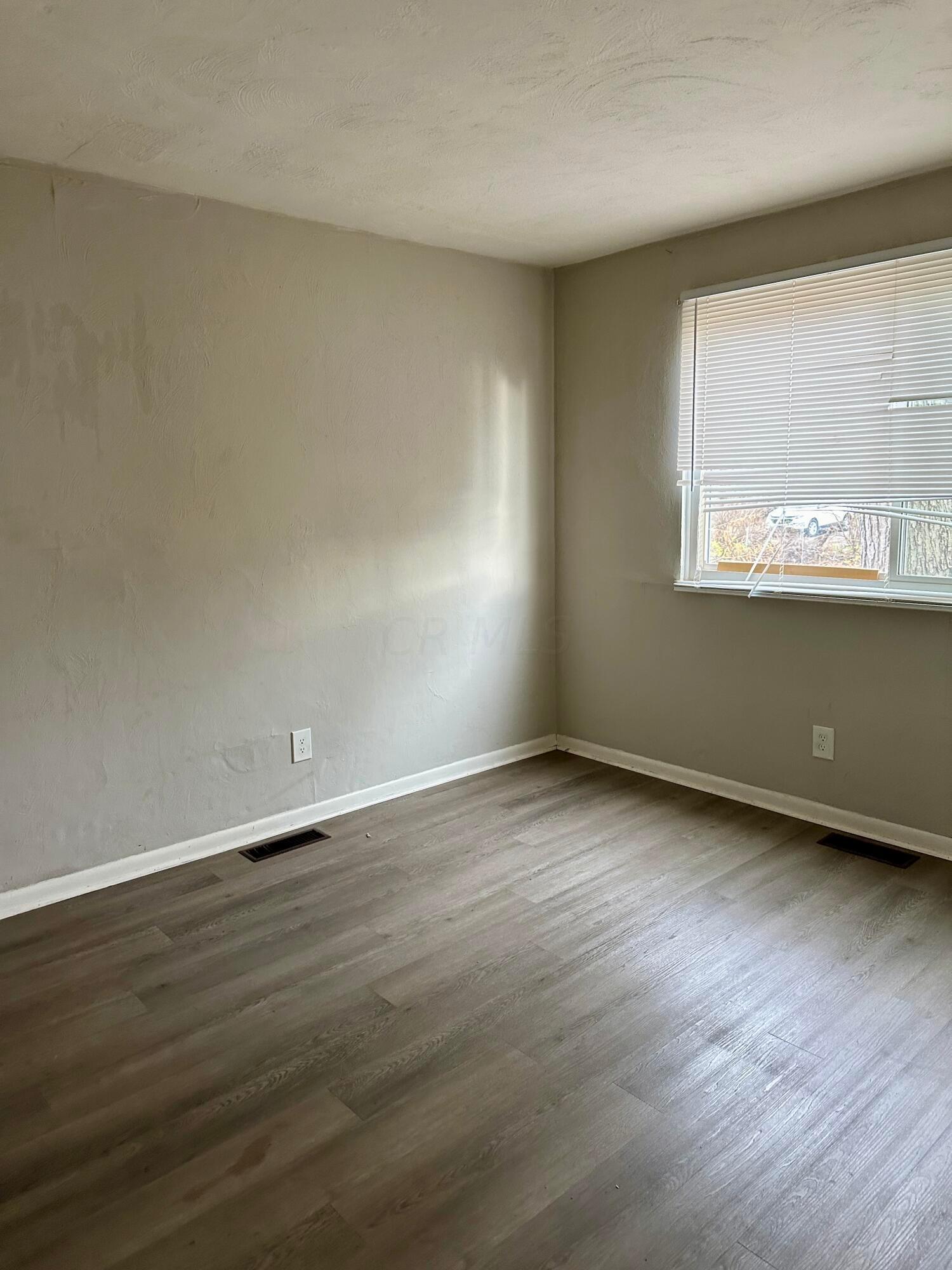 Empty room with gray-brown plank flooring and a window with white blinds.