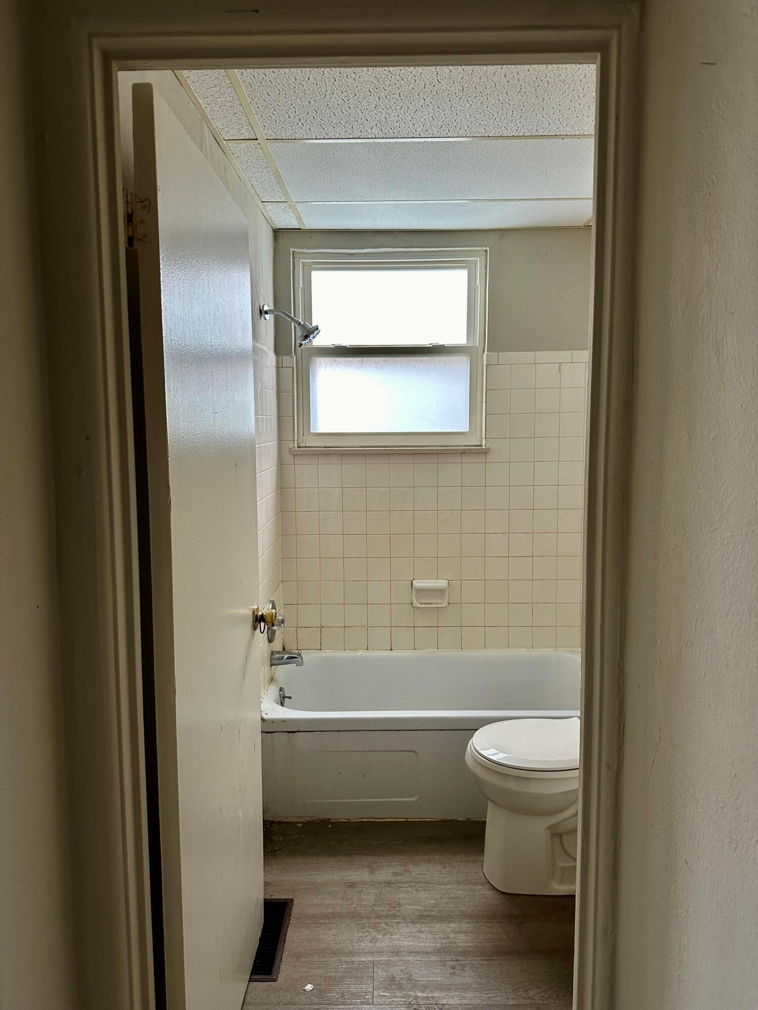 Bathroom with tiled tub and shower, toilet, and window above the tub.
