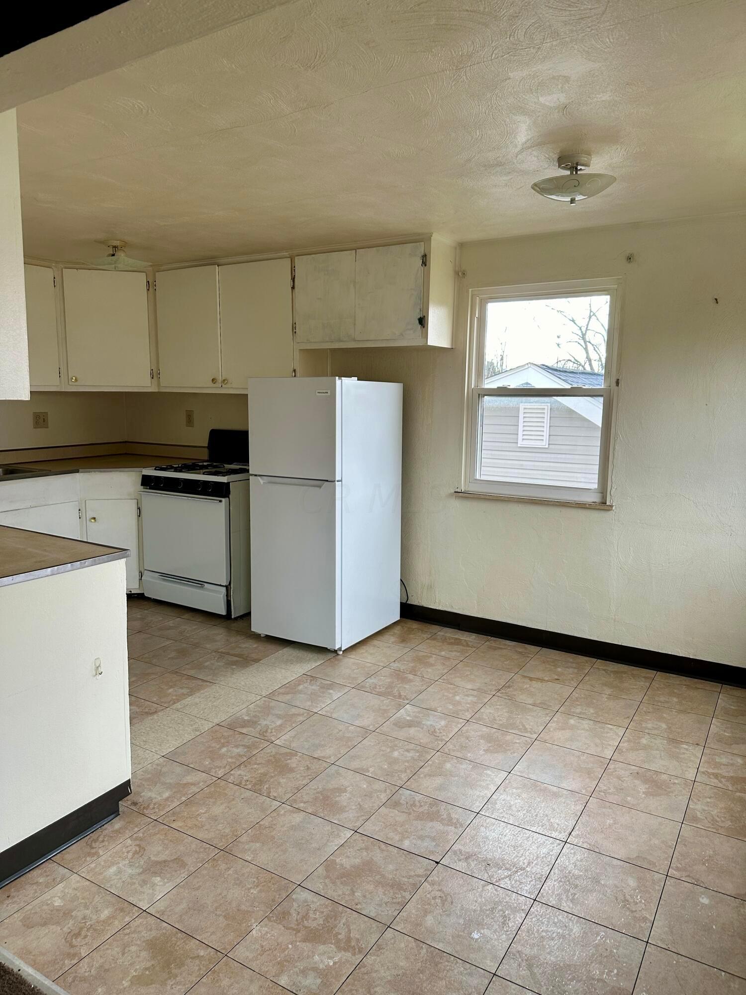 Kitchen with white cabinets, a gas stove, refrigerator, and tan tile flooring.