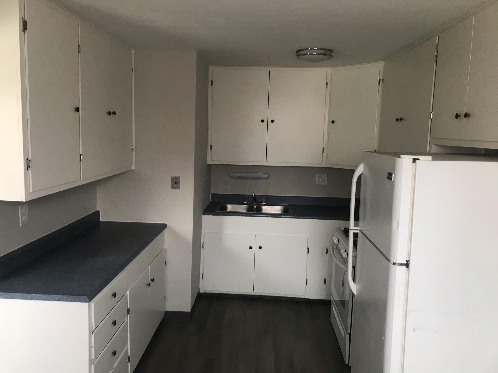 Kitchen with white cabinets, dark countertops, a double-basin sink, and white appliances.