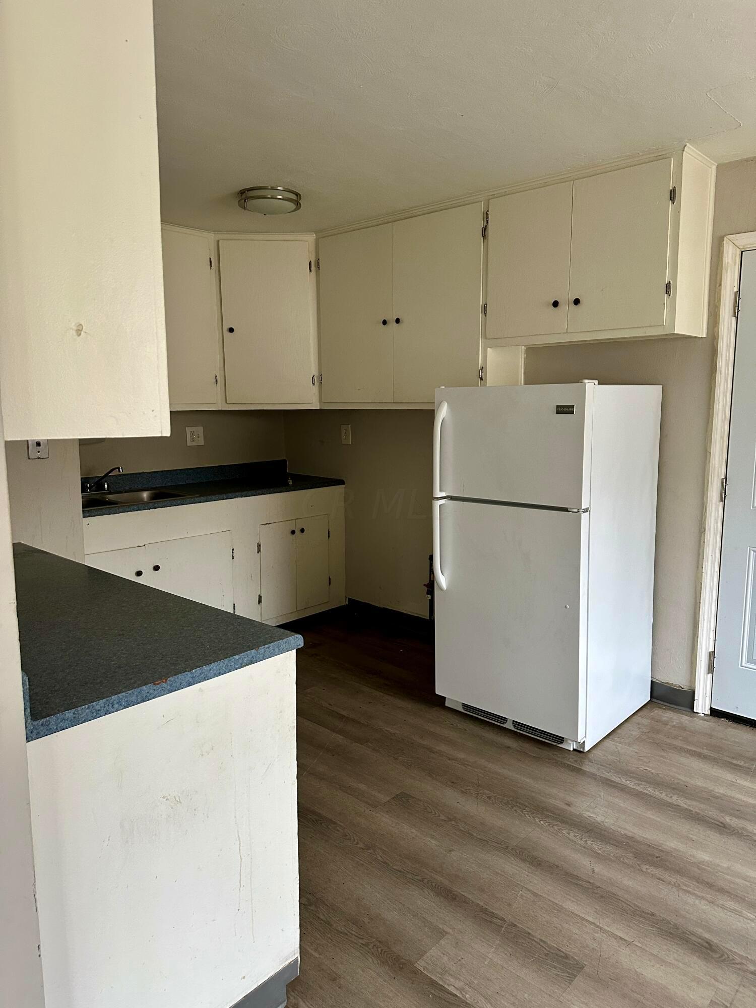Unfurnished kitchen with cream cabinets, a dark countertop, sink, and white refrigerator.