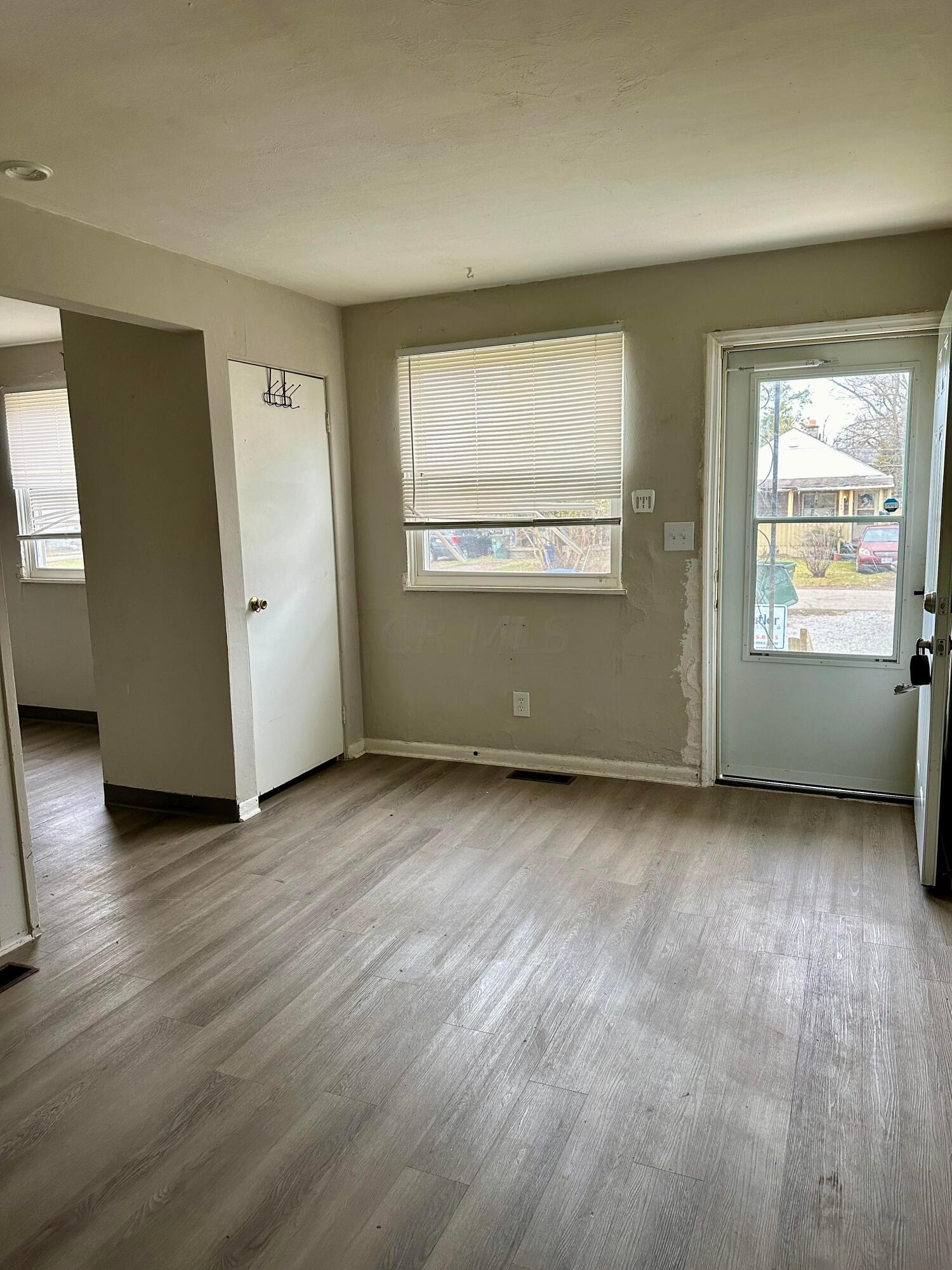 Empty room with gray wood-look floors, window blinds, and a glass exterior door.