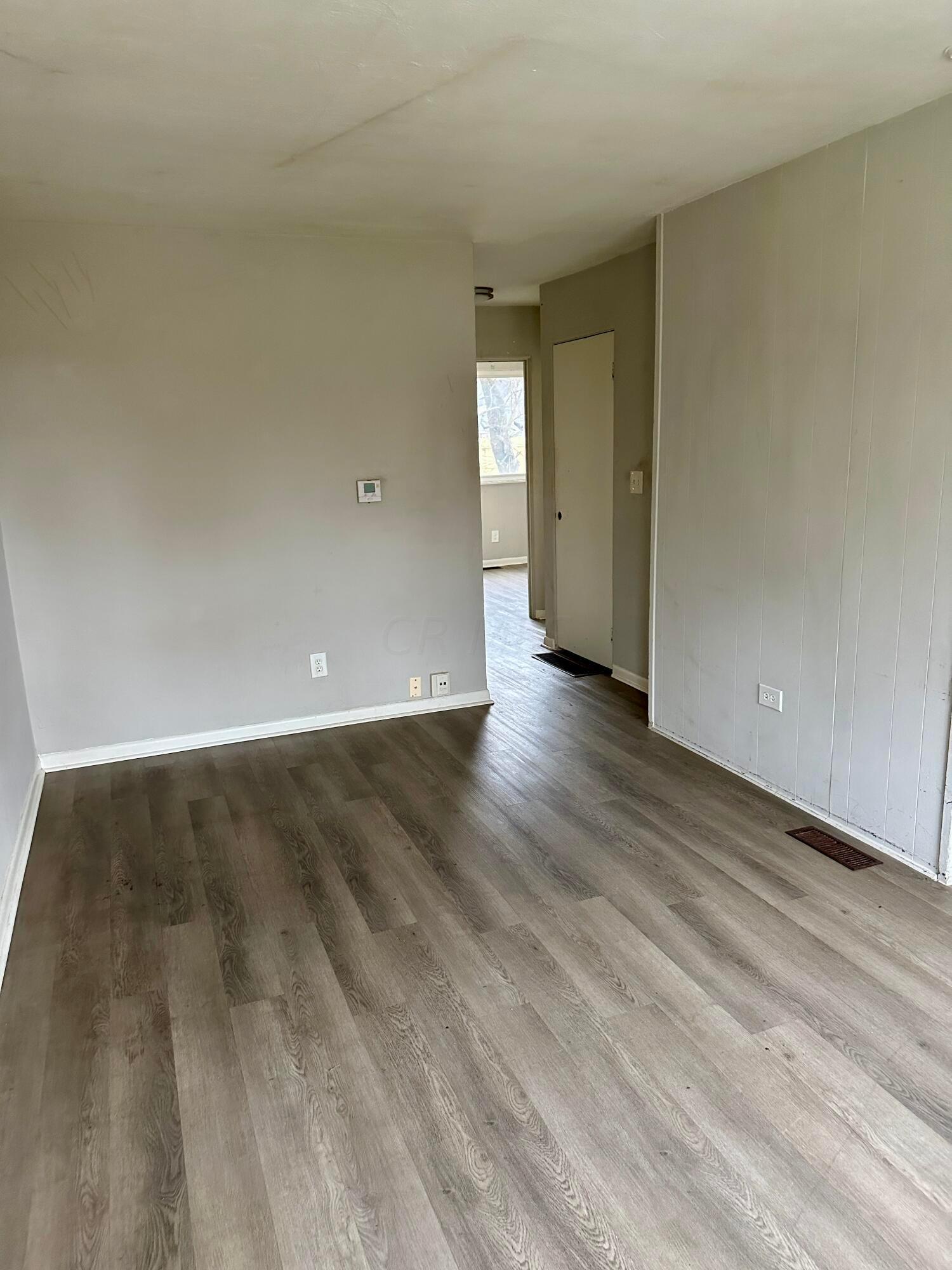Empty room with gray-brown plank flooring and an opening to a hallway.
