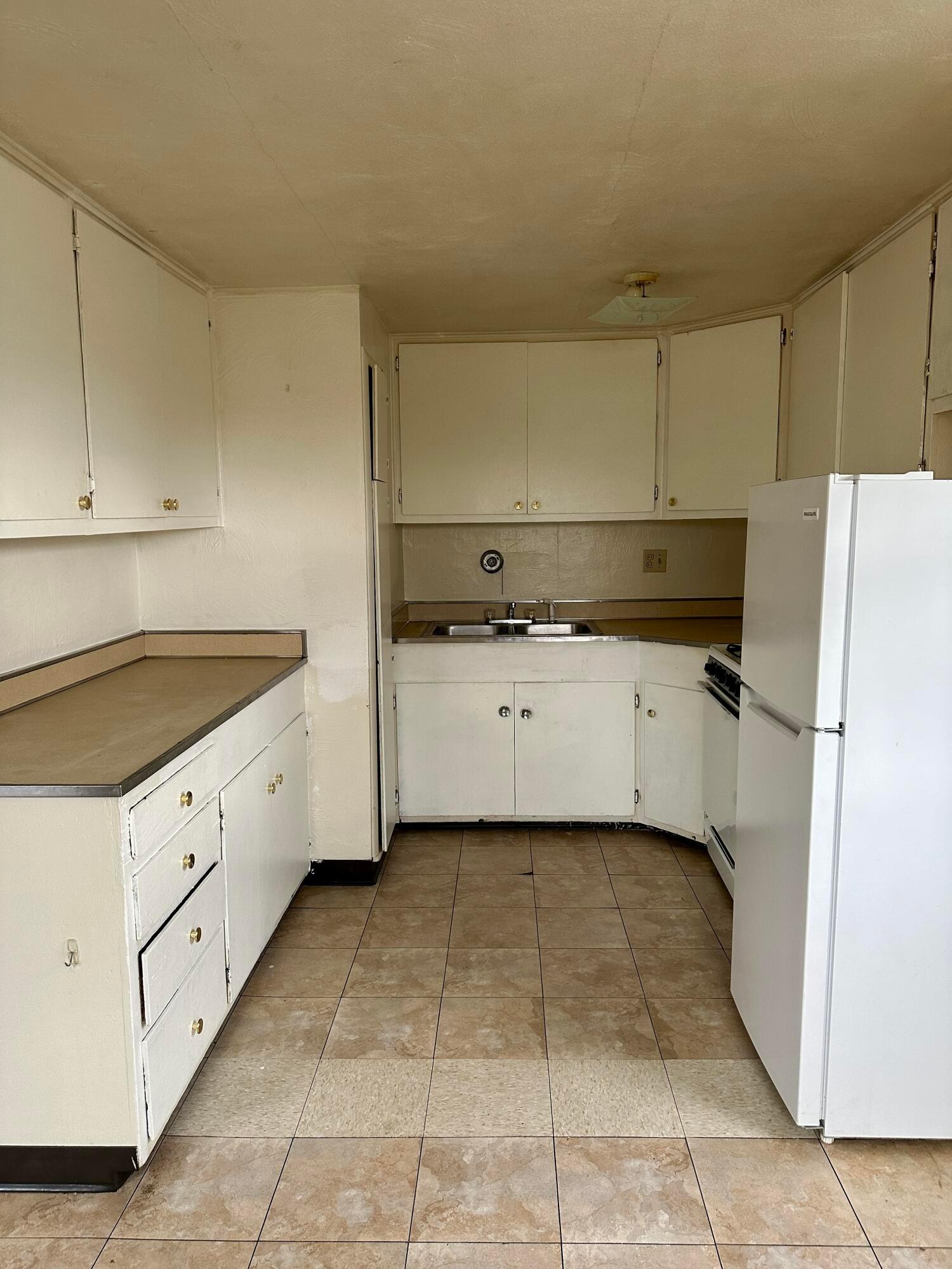 Kitchen with white cabinets, tan countertops, a double sink, and brown tile flooring.
