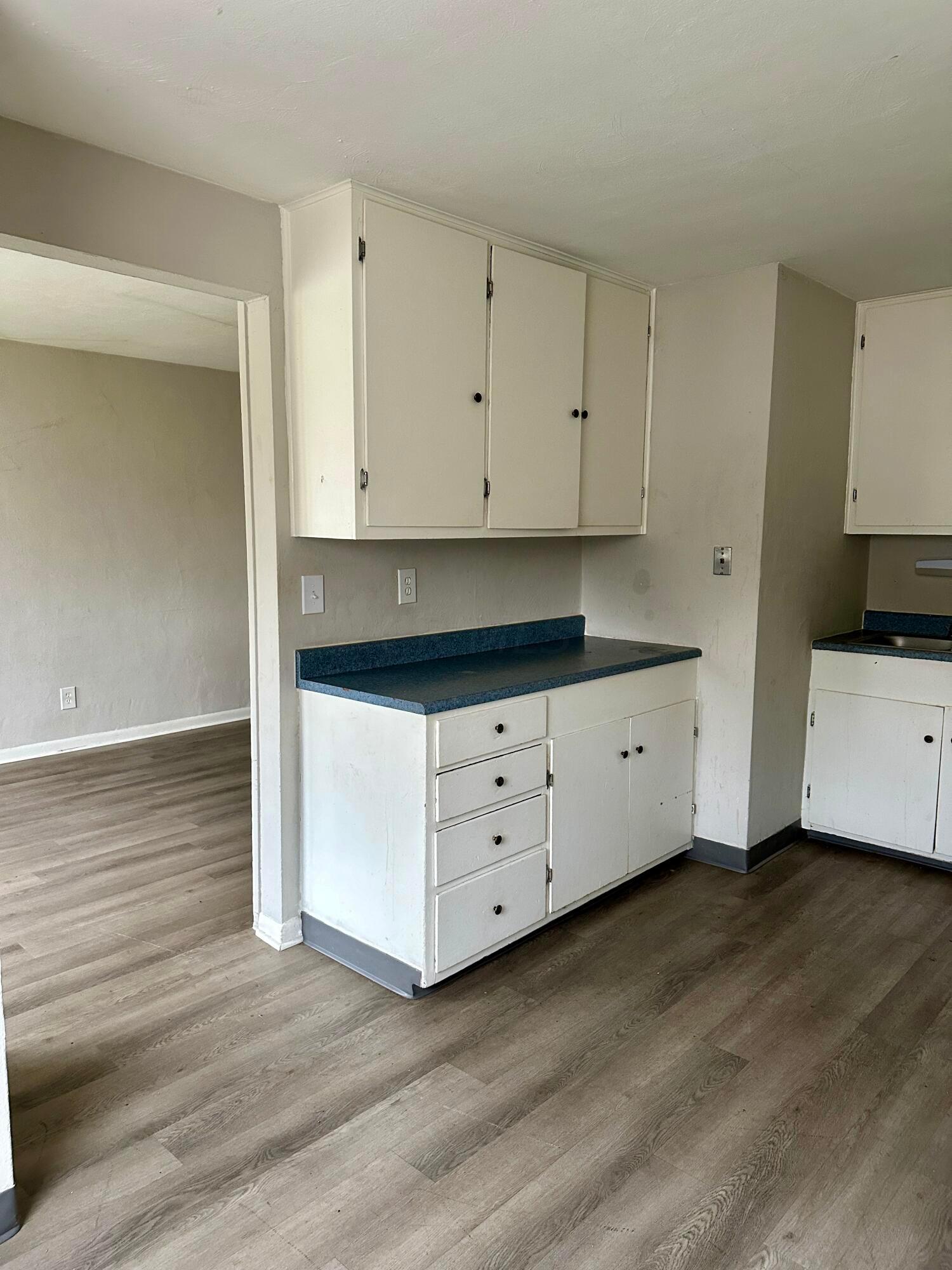 Kitchen with white cabinets, blue countertops, and wood-look flooring beside an open doorway.