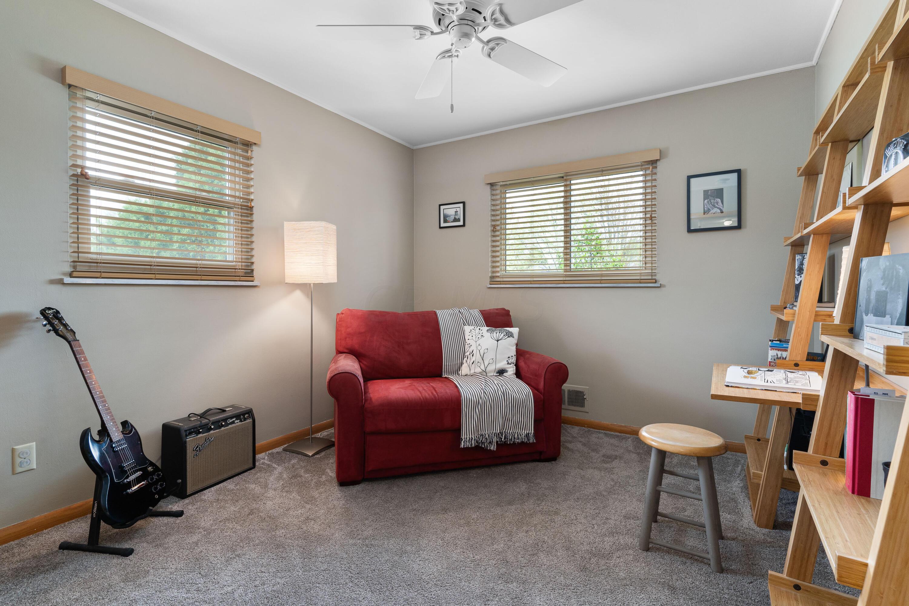 Furnished sitting room with a red loveseat, guitar and amplifier, and tall wooden shelving.