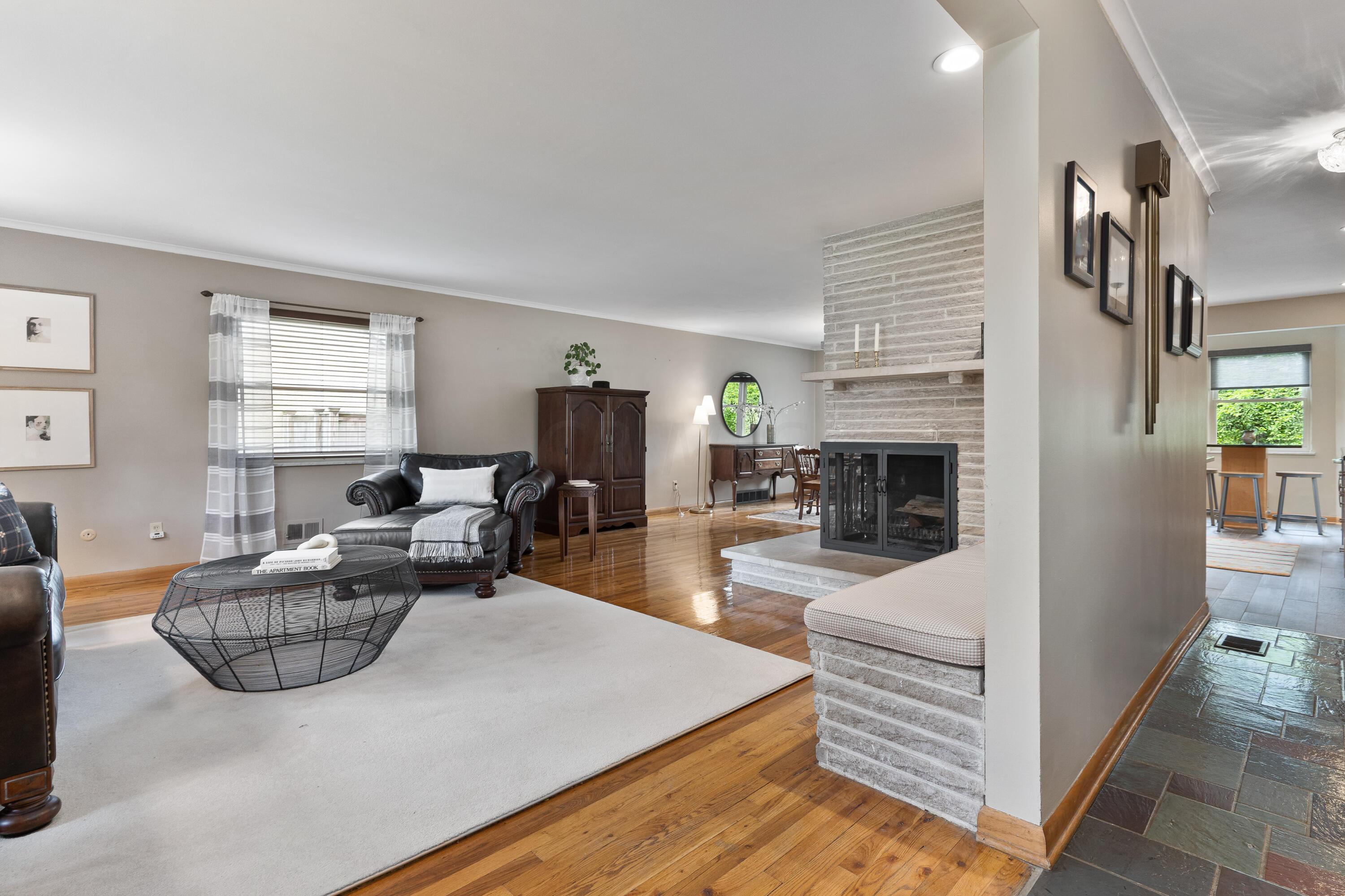Living room with a whitewashed brick fireplace, leather seating, and hardwood floors.