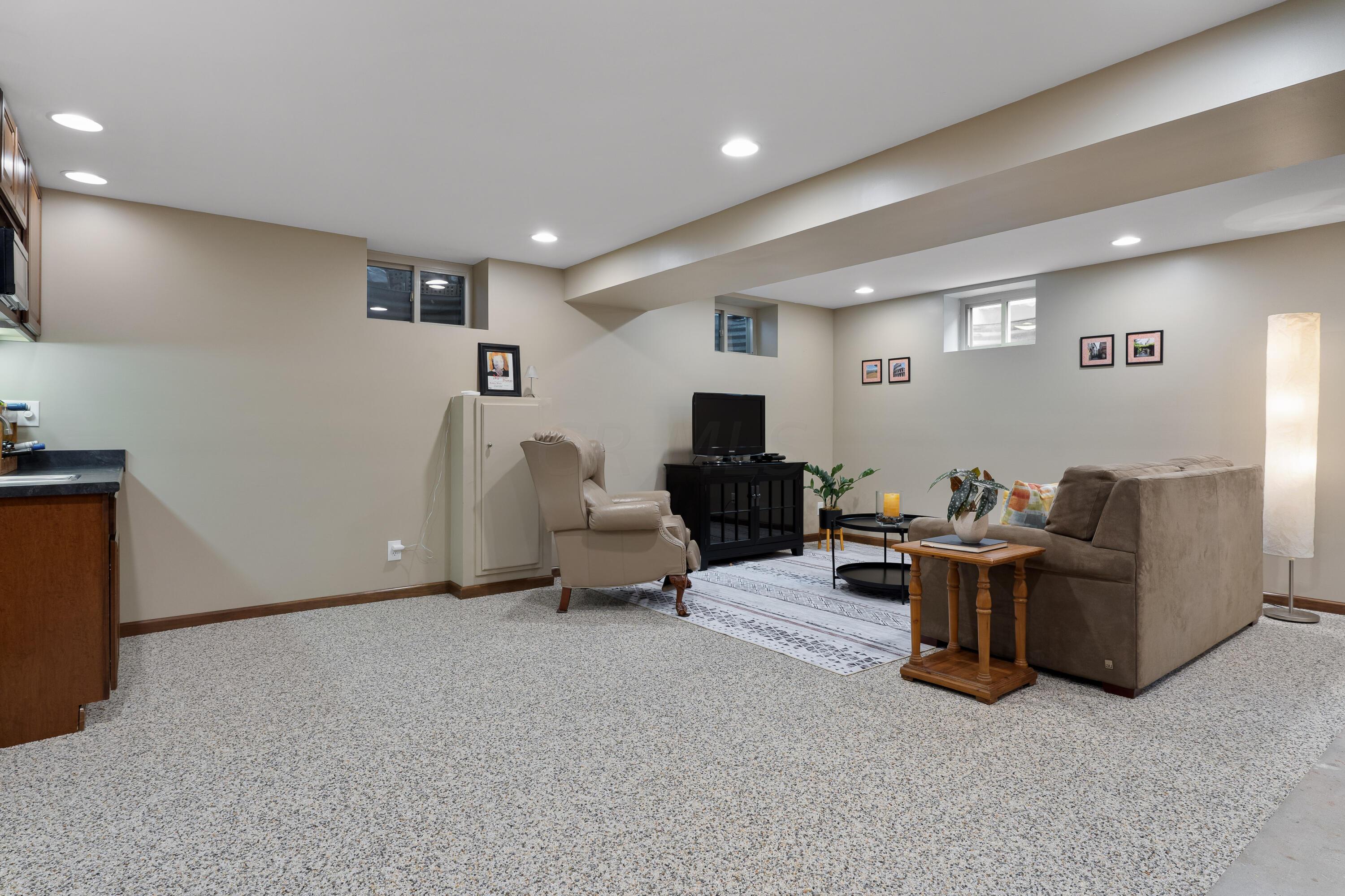Lower-level living room with beige seating, a television, and speckled carpet.