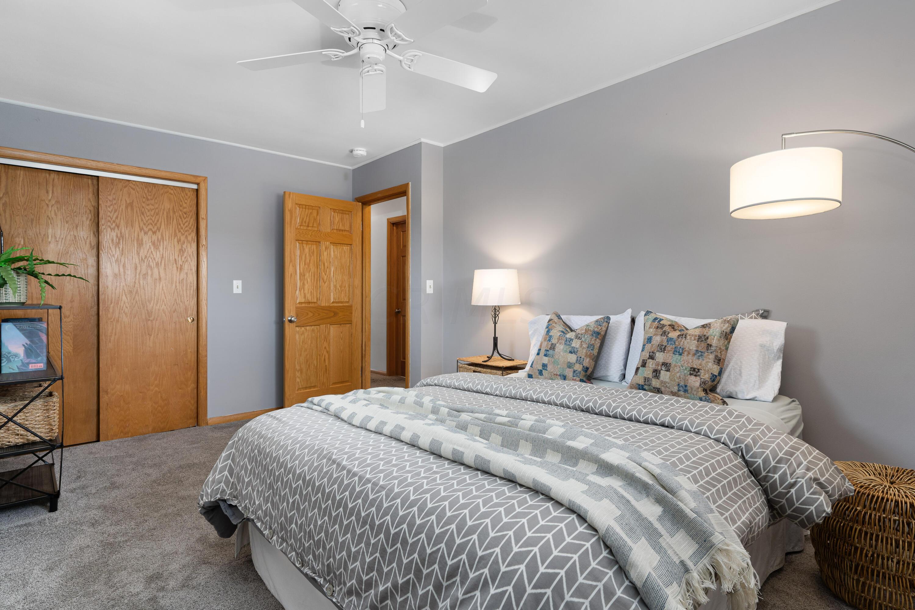 Staged bedroom with gray patterned bedding, colorful accent pillows, and wood closet doors.