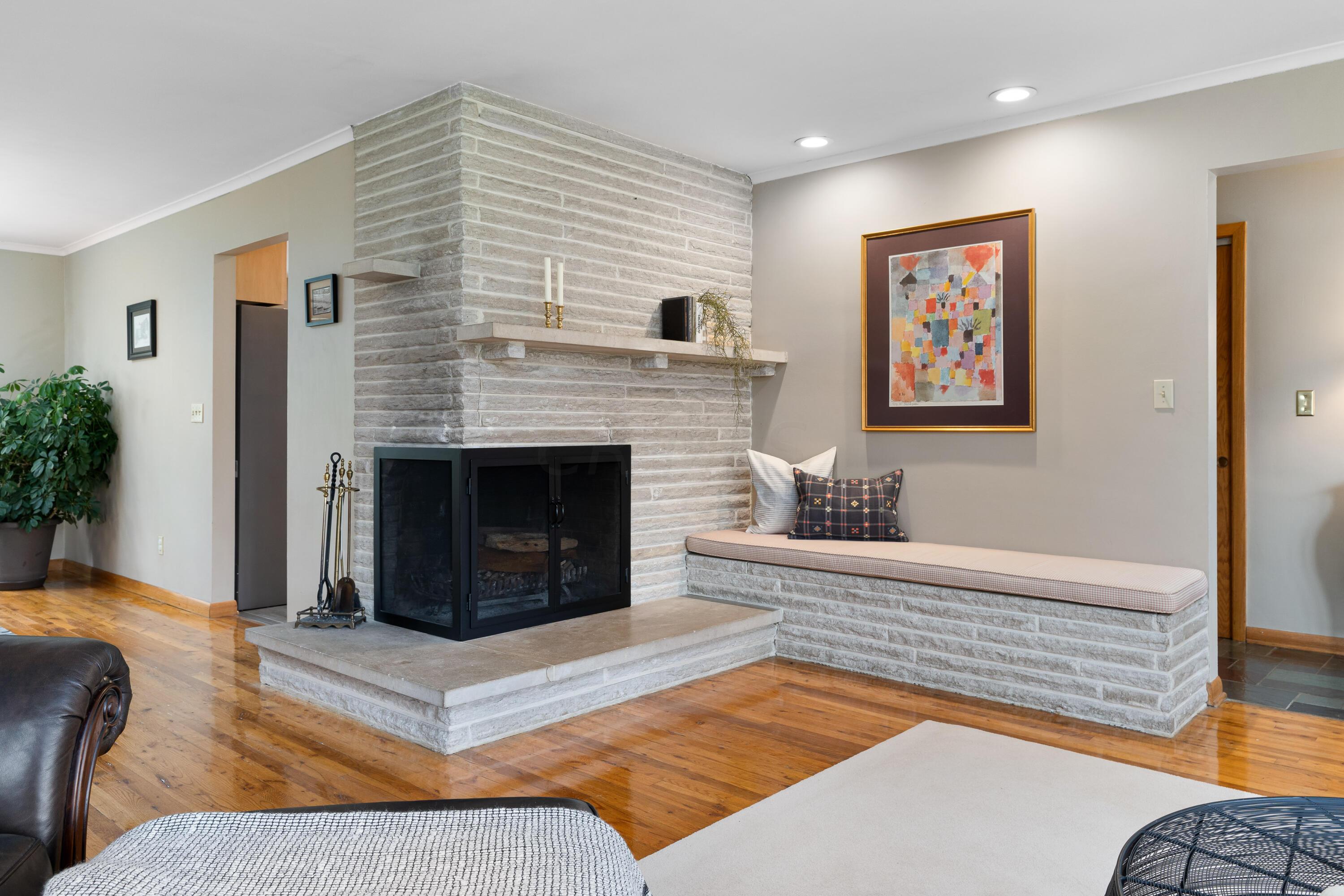 Living room with a whitewashed brick fireplace, raised hearth, and built-in cushioned window seat.
