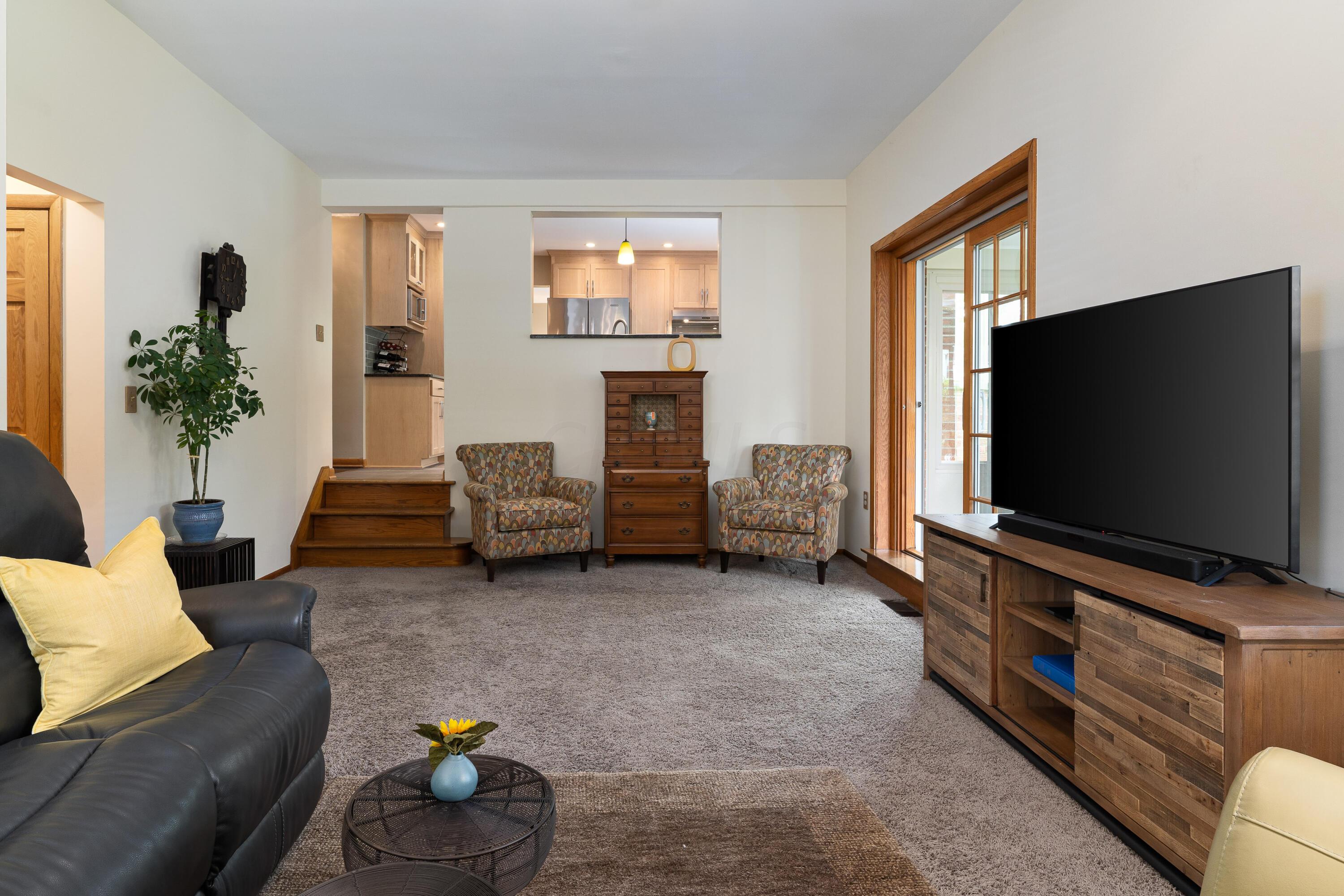 Living room with patterned armchairs, wooden media console, and an open view into the kitchen.