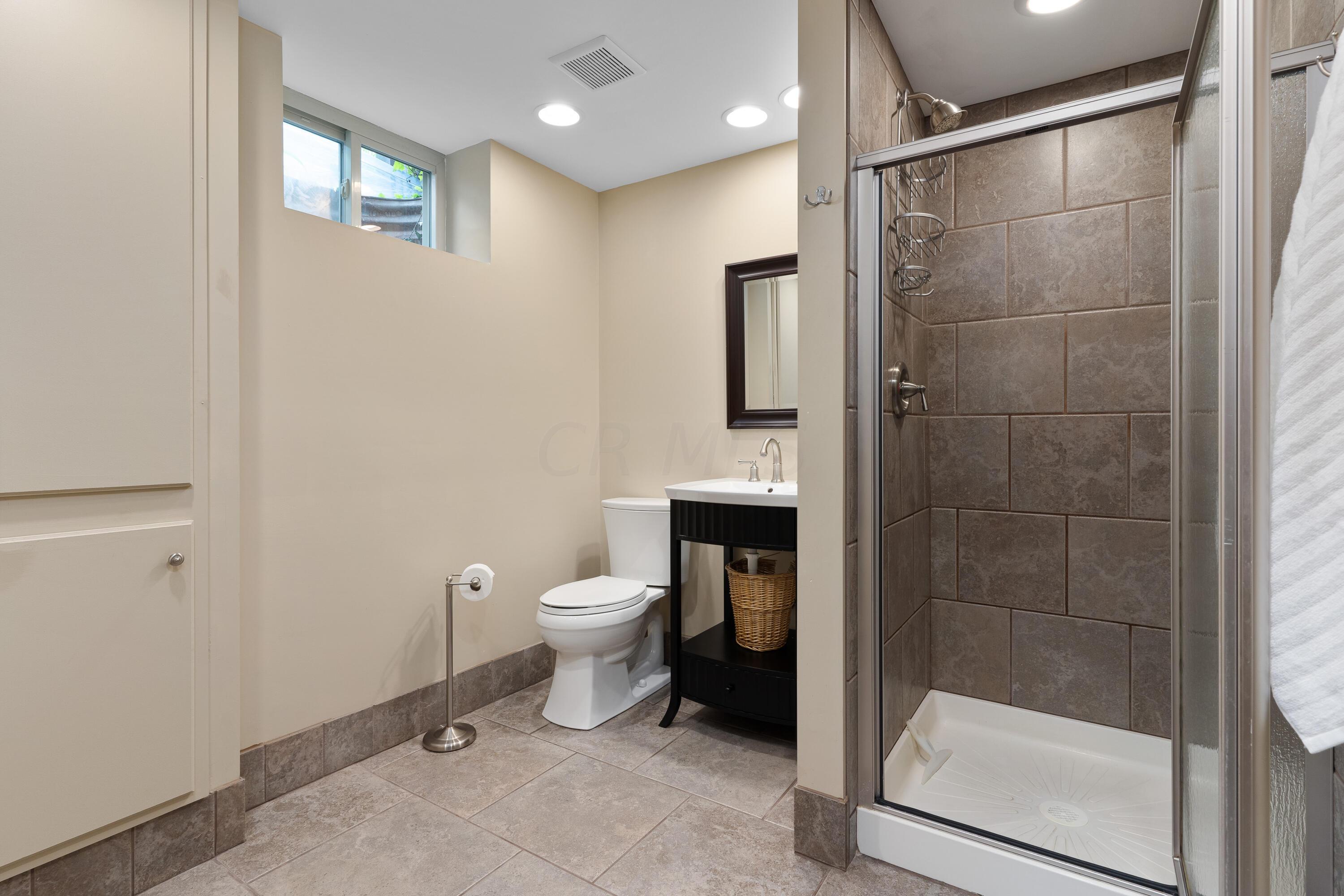 Bathroom with a tiled glass-enclosed shower, black vanity, and high windows.