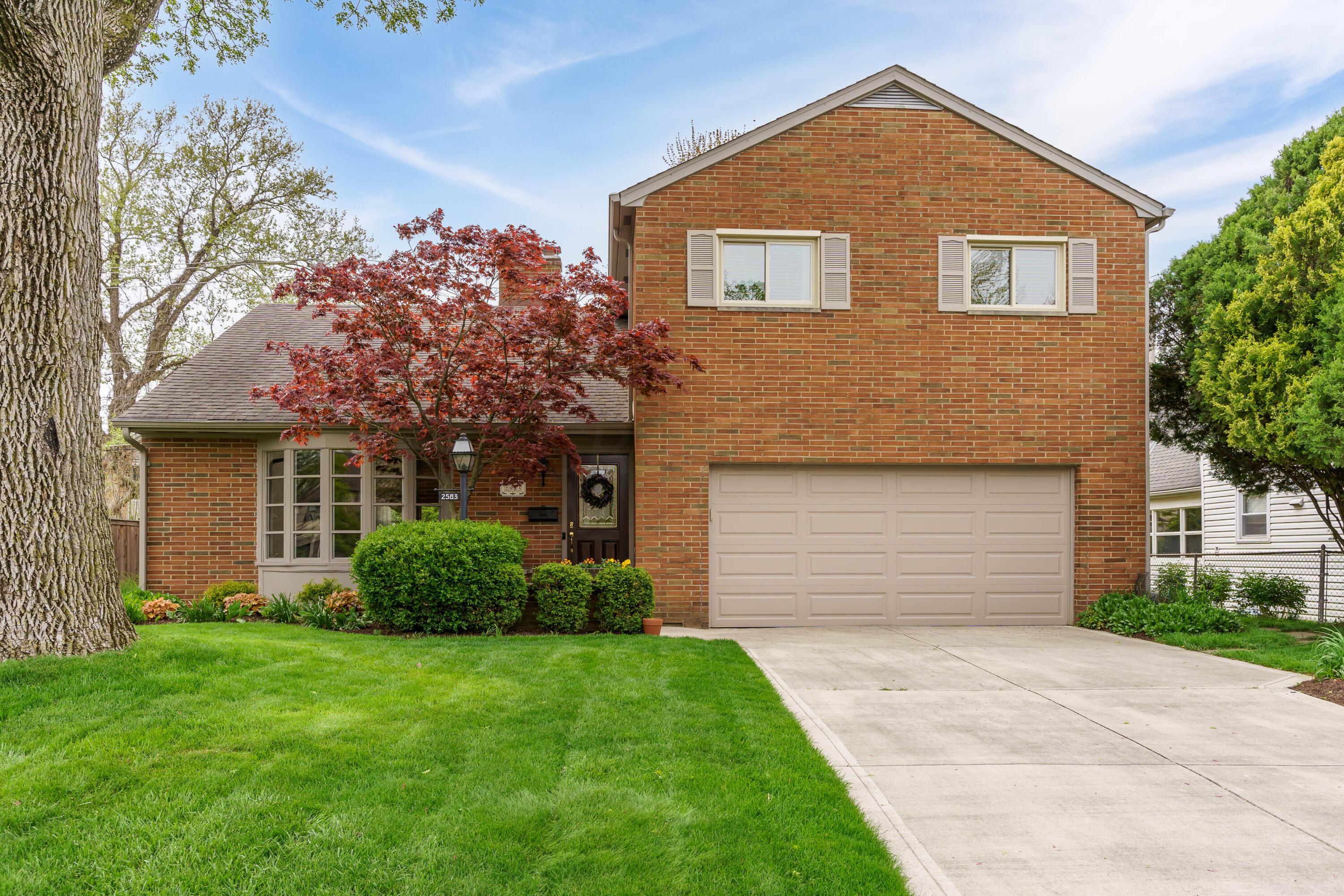 Two-story brick home with an attached garage, bay window, and red-leaf tree by the entrance.