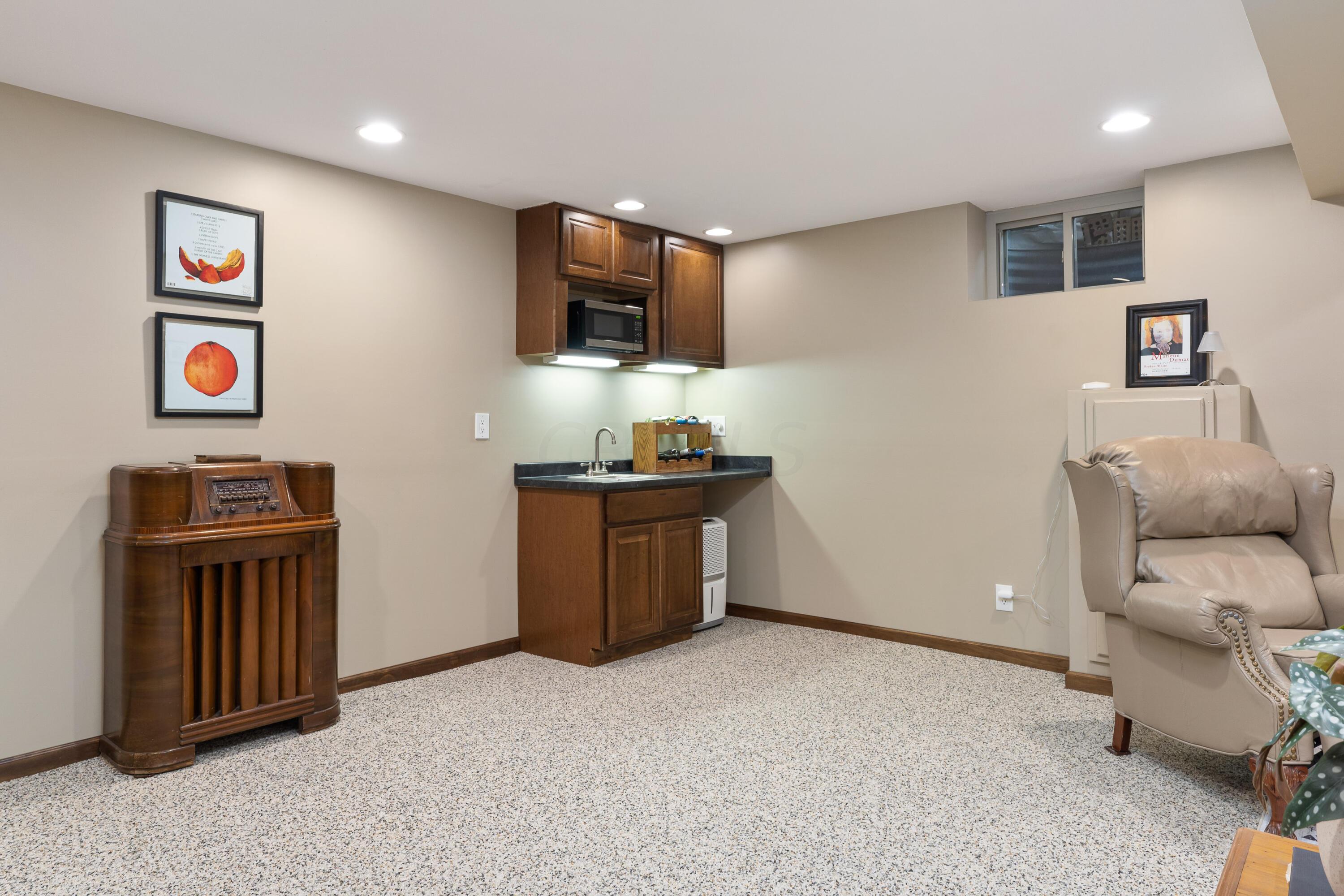 Basement rec room with a compact wood-cabinet wet bar, vintage radio, and beige leather recliner.