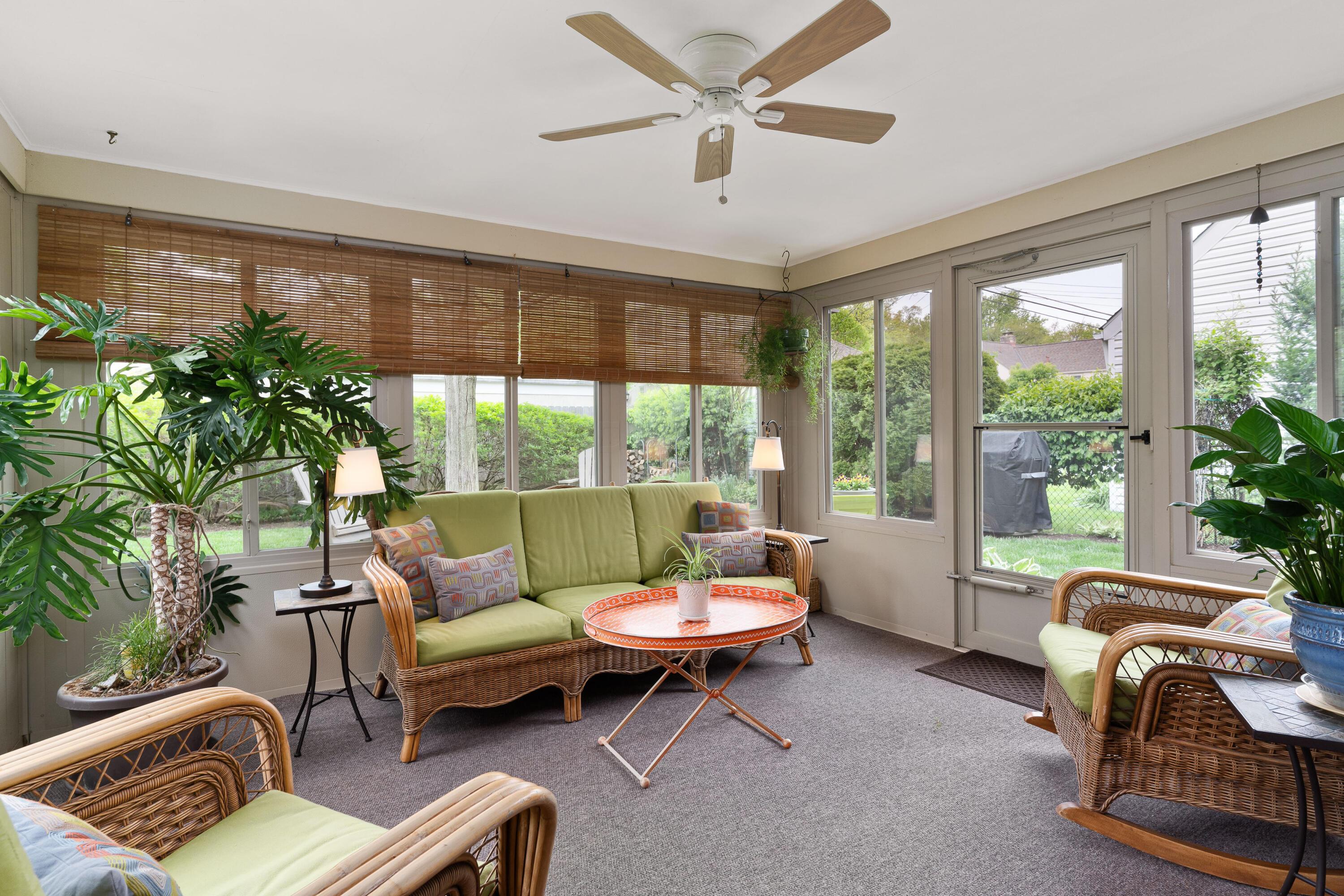 Sunroom with wicker seating, a patterned coffee table, large windows, and leafy plants.