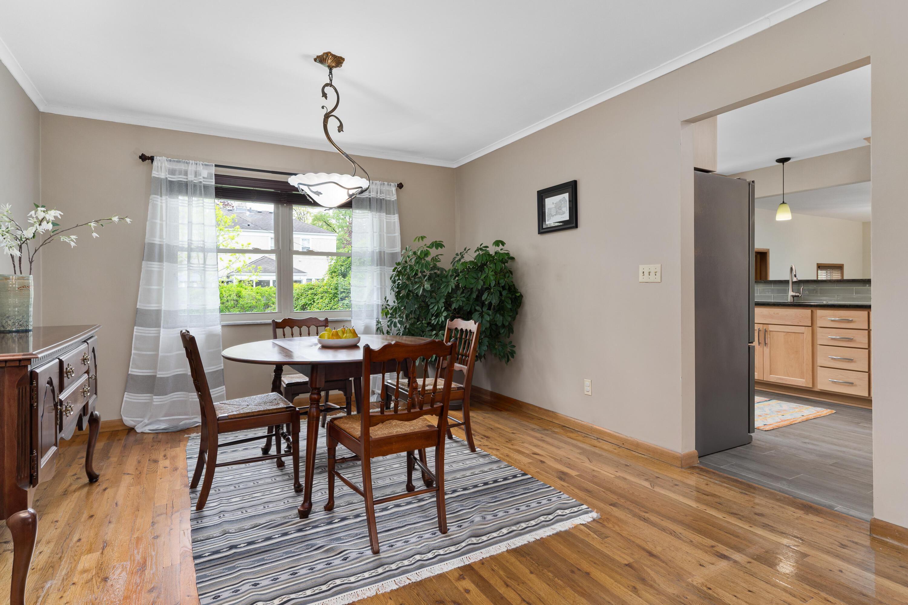 Dining room with a dark wood table, striped rug, hardwood floors, and a view into the kitchen.