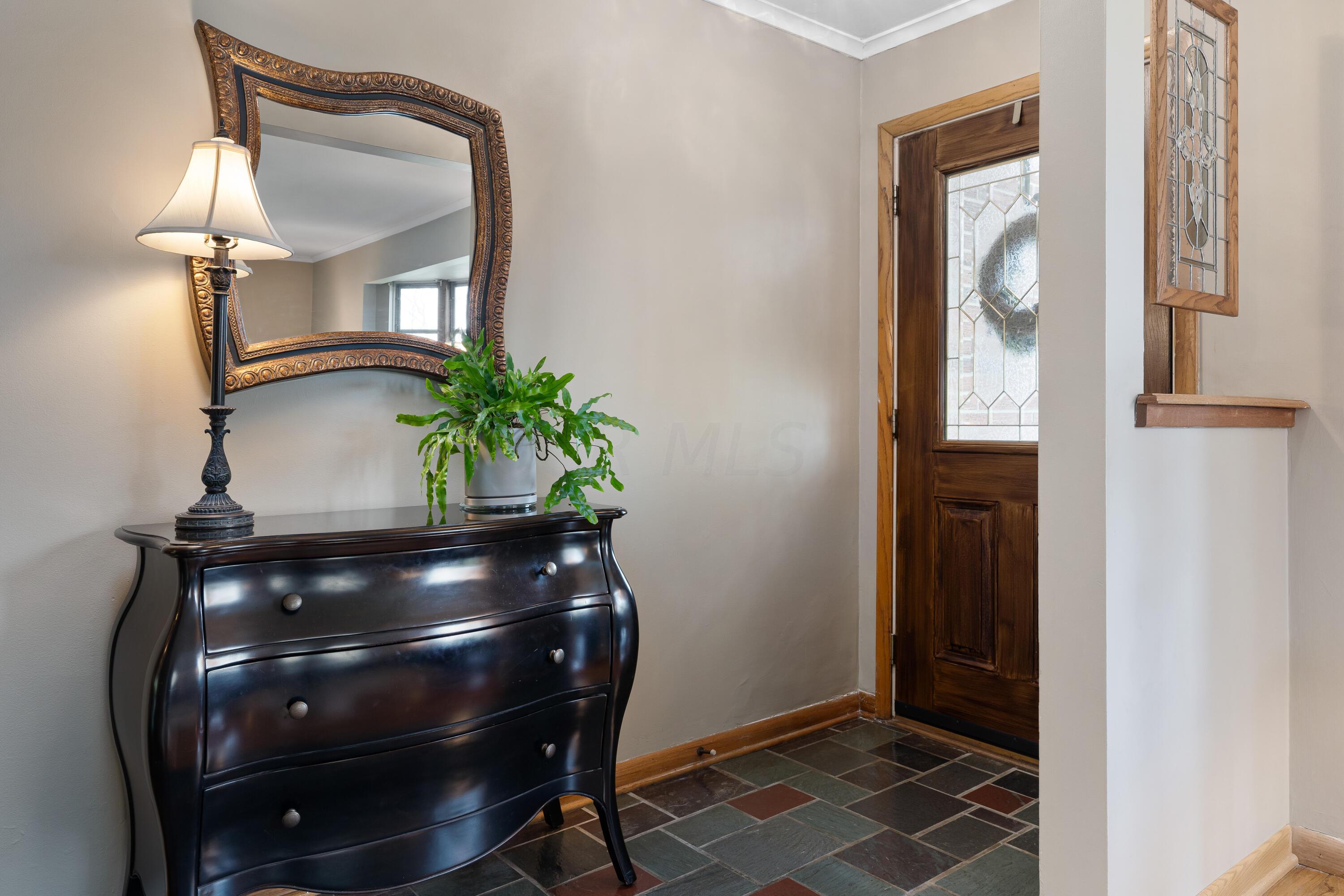 Entryway with dark dresser, ornate mirror, and wood front door with decorative glass.